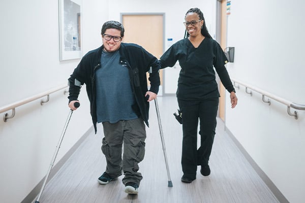 A Rehabilitation patient smiling while walking with crutches