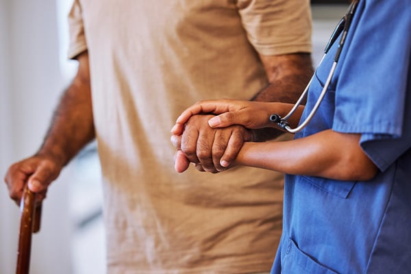 An elderly man walking supported by his healthcare provider