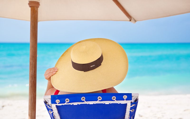 A woman relaxing on the beach wearing a large hat and staying in the shade