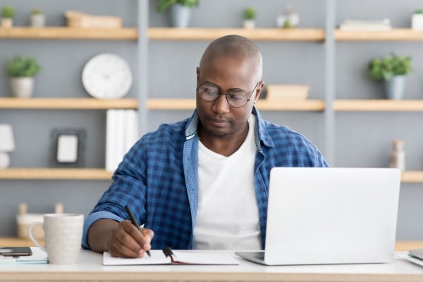 man taking notes by a laptop