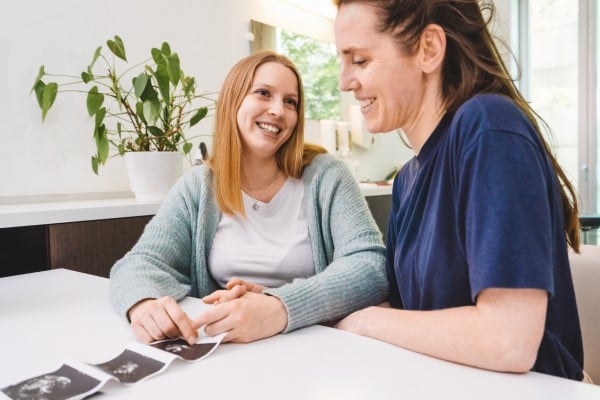 Two women partners celebrate ultrasound printouts showing successful fertilization