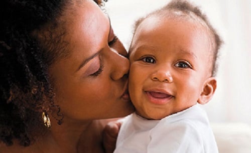 A smiling baby getting a kiss from mom